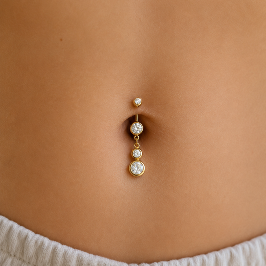 Photo portée d'un piercing nombril en acier chirurgical doré avec pendentif de trois oxydes de zirconium, barre 1,6 x 10 mm.