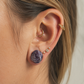 Plug d'oreille en agathe violette sculptée en forme de rose, porté sur le lobe. Écarteur en pierre naturelle aux nuances violettes et grises avec finition polie brillante.